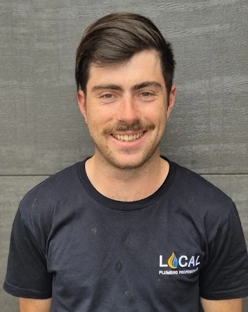 Portrait of Lachie, a friendly plumber in a black Local Plumbing Professionals t-shirt, standing by a gray wall.