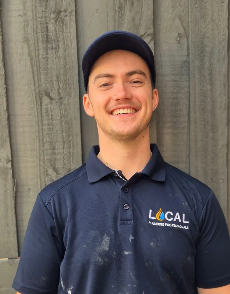 Portrait of Nick, a smiling plumber in a navy Local Plumbing Professionals uniform, standing by a wooden background.