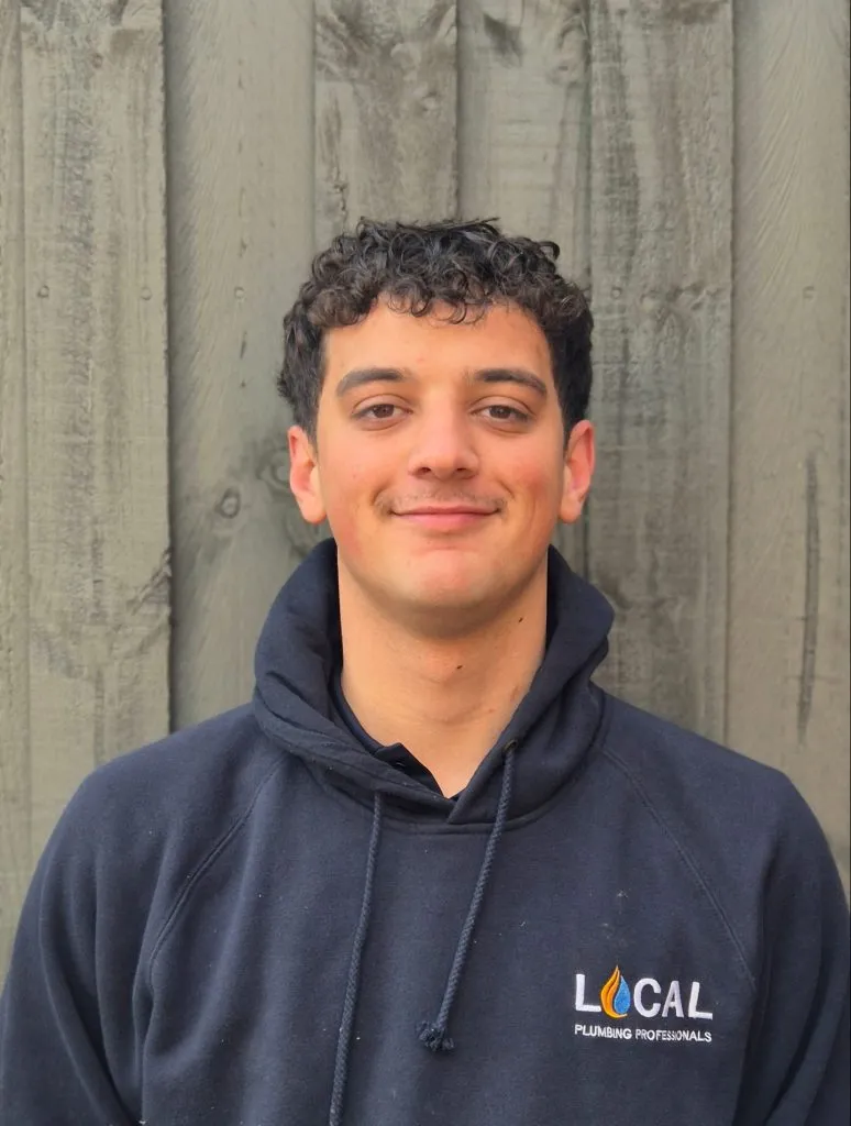Portrait of Ryan, a professional plumber wearing a navy Local Plumbing Professionals hoodie, standing against a wooden background.